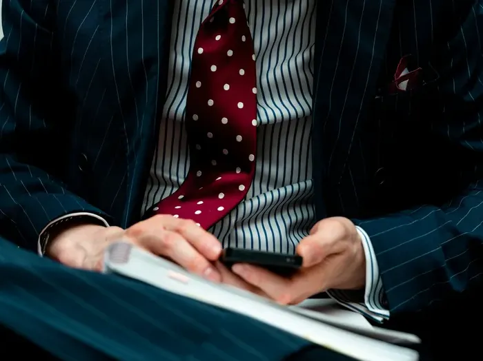 Business professional in a pinstripe suit with a red polka dot tie, using a smartphone while reviewing notes